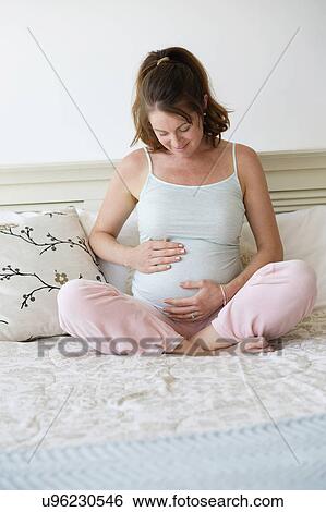 Smiling pregnant woman sitting on bed View Large Photo Image Stock Photograph - Smiling pregnant woman sitting on bed. Fotosearch