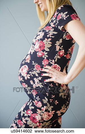 Stock Image - Studio shot of pregnant woman in floral dress. Fotosearch