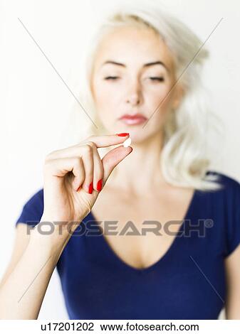 Stock Image - Studio shot of woman holding pill. Fotosearch