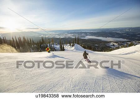 Stock Photo - Two people on ski slope at sunlight. Fotosearch