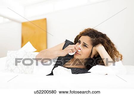 Stock Image - Woman blowing nose in bed. Fotosearch
