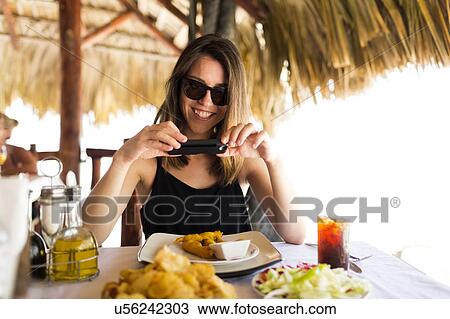 Stock Image - Woman by table, using phone. Fotosearch