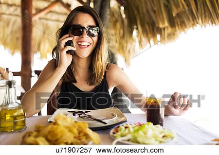 Stock Photo - Woman by table, using phone. Fotosearch