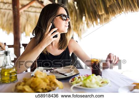 Stock Photograph - Woman by table, using phone. Fotosearch