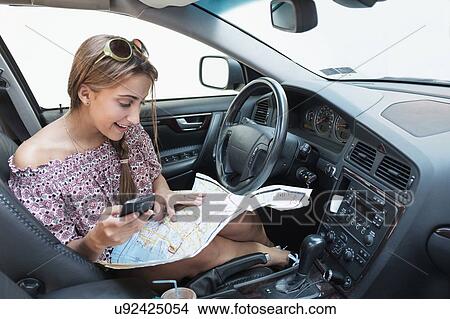 Picture - Woman checking phone in car with map on lap. Fotosearch