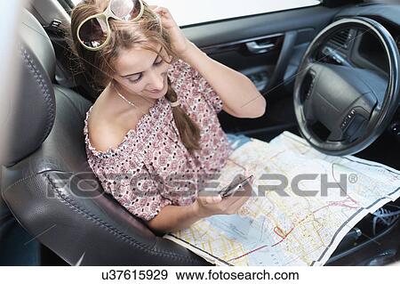 Stock Photo - Woman checking phone in car with map on lap. Fotosearch
