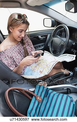 Woman checking phone in car with map on lap View Large Photo Image Stock Photo - Woman checking phone in car with map on lap. Fotosearch