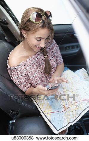 Woman checking phone in car with map on lap View Large Photo Image Stock Photo - Woman checking phone in car with map on lap. Fotosearch