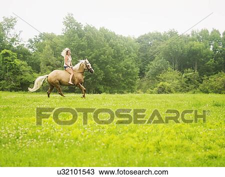 Stock Image - Woman horseback riding in countryside. Fotosearch