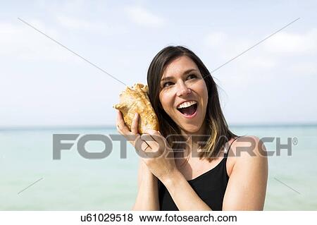 Woman listening to seashell View Large Photo Image Stock Photo - Woman listening to seashell. Fotosearch