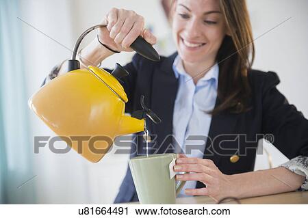 Stock Image - Woman making tea in office. Fotosearch