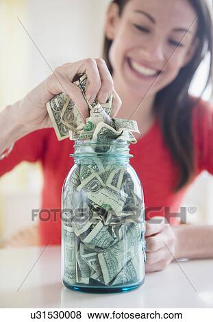 Stock Photo - Woman putting money into jar. Fotosearch