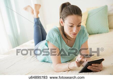 Stock Image - Woman shopping online in bed. Fotosearch