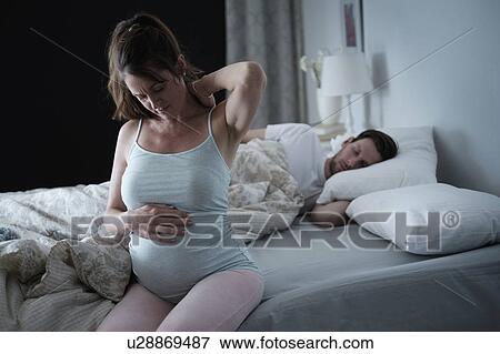 Stock Photo - Woman sitting on bed and stretching stiff neck. Fotosearch