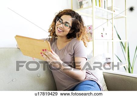 Woman sitting on sofa, using digital tablet View Large Photo Image Stock Photo - Woman sitting on sofa, using digital tablet. Fotosearch