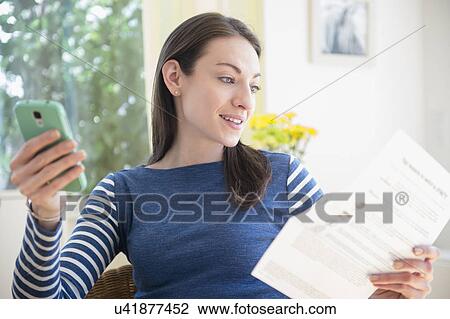 Stock Image - Woman with document and Smartphone at home. Fotosearch