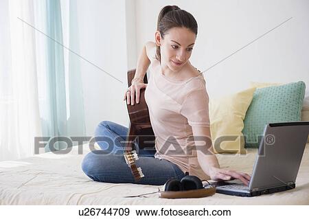 Stock Photo - Woman with laptop and guitar on bed. Fotosearch