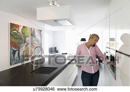 Stock Photograph - Woman with laptop in kitchen. Fotosearch