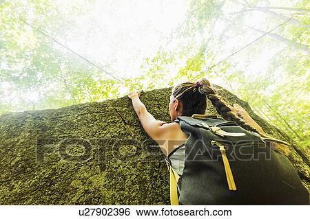 Stock Photograph - Young woman climbing on rock in forest. Fotosearch