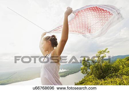 Stock Photograph - Young woman holding scarf on wind against lake view. Fotosearch