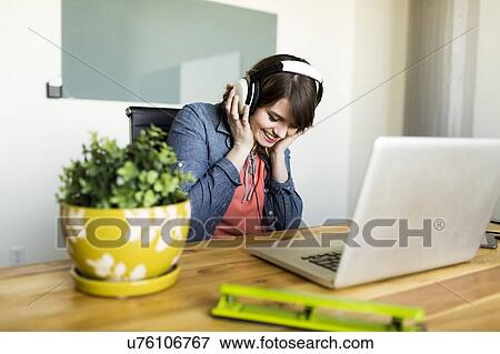Young woman listening to music in office View Large Photo Image Stock Photo - Young woman listening to music in office. Fotosearch