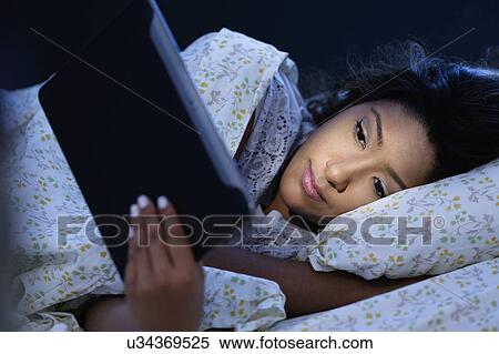 Stock Photography - Young woman lying in bed, using digital tablet. Fotosearch