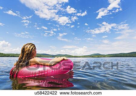 Stock Image - Young woman relaxing on lake in pool raft. Fotosearch