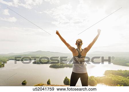 Stock Photo - Young woman standing on top of mountain with outstretched arms, rear view. Fotosearch