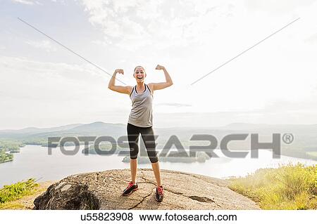 Young woman standing on top of mountain and flexing muscles View Large Photo Image Stock Photo - Young woman standing on top of mountain and flexing muscles. Fotosearch
