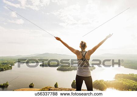 Young woman standing on top of mountain with outstretched arms, rear view View Large Photo Image Stock Photo - Young woman standing on top of mountain with outstretched arms, rear view. Fotosearch