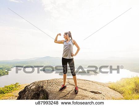 Young woman standing on top of mountain and flexing muscles View Large Photo Image Stock Photo - Young woman standing on top of mountain and flexing muscles. Fotosearch