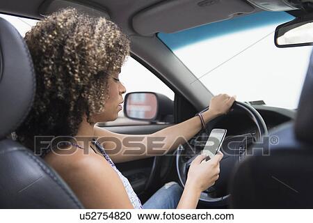 Stock Image - Young woman texting while driving car. Fotosearch