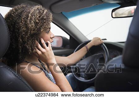 Picture - Young woman using phone while driving car. Fotosearch