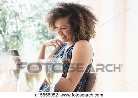 Stock Image - Young woman using smart phone at restaurant. Fotosearch