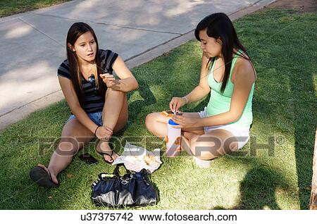 Stock Image -  girls teen teenager sitting in grass talking. Fotosearch
