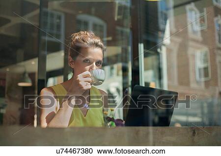 Stock Image - A young brunette woman sitting in a cafe working. Fotosearch