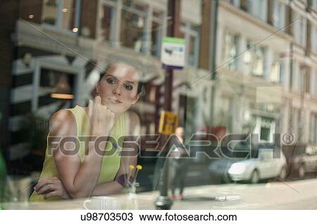 Stock Image - A young brunette woman sitting in a cafe looking out of the window. Fotosearch