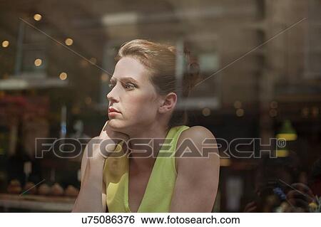 Stock Photograph - A young brunette woman sitting in a cafe looking out of the window. Fotosearch