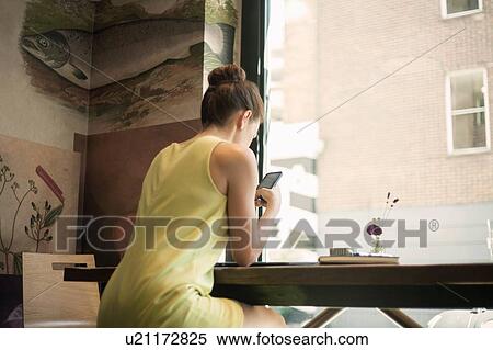 A young brunette women sitting in a cafe texting and holding mobile phone View Large Photo Image Stock Photography - A young brunette women sitting in a cafe texting and holding mobile phone. Fotosearch