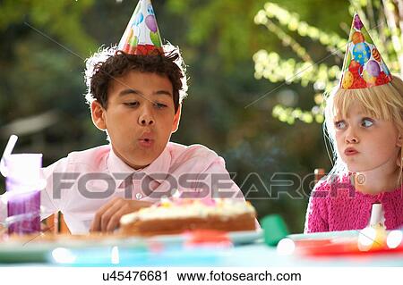 Stock Image - Boy blowing candles on birthday cake at garden birthday party. Fotosearch