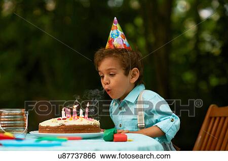Stock Photograph - Boy blowing candles on birthday cake at garden birthday party. Fotosearch