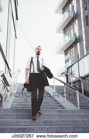 Stock Photo - Businessman carrying jacket moving down city stairway. Fotosearch