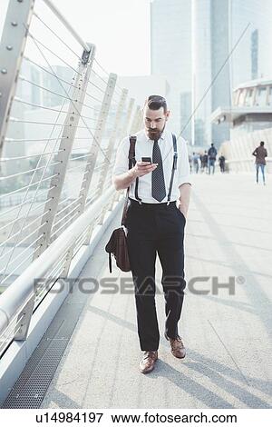 Businessman reading smartphone text update whilst walking on footbridge View Large Photo Image Stock Photo - Businessman reading smartphone text update whilst walking on footbridge. Fotosearch