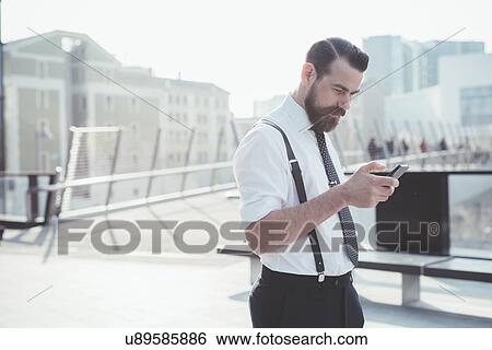 Businessman reading smartphone update on footbridge View Large Photo Image Stock Photograph - Businessman reading smartphone update on footbridge. Fotosearch