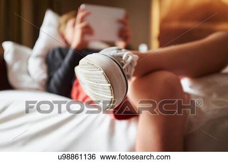 Close up of teenage boys trainer whilst he reclines on bed using digital tablet View Large Photo Image Stock Photograph - Close up of teenage boys trainer whilst he reclines on bed using digital tablet. Fotosearch