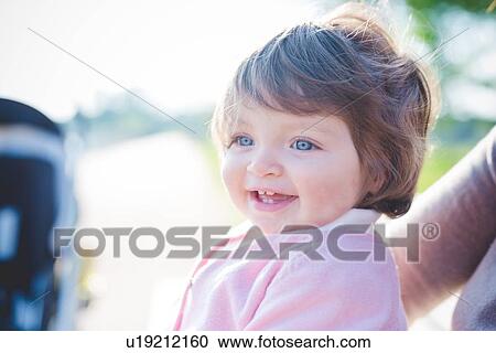 Stock Image - Close up portrait of blue eyed female toddler in park. Fotosearch