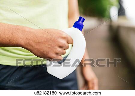 Stock Image - Cropped shot of male runner holding water bottle. Fotosearch