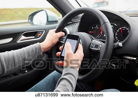 Stock Photo - Cropped shot of man using smartphone whilst driving. Fotosearch