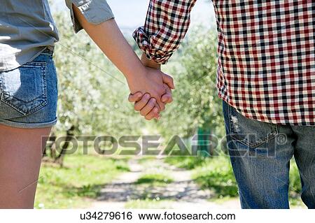 Cropped view of couple holding hands looking down dirt track View Large Photo Image Stock Photograph - Cropped view of couple holding hands looking down dirt track. Fotosearch