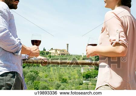 Stock Photograph - Cropped view of young couple face to face holding wine glasses. Fotosearch